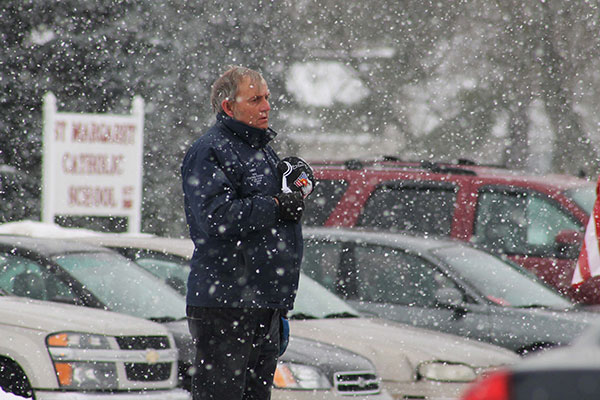 Reporter holds a microphone during heavy snowfall in a parking lot.