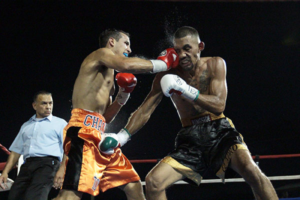 Two boxers exchange punches in a ring while a referee watches.