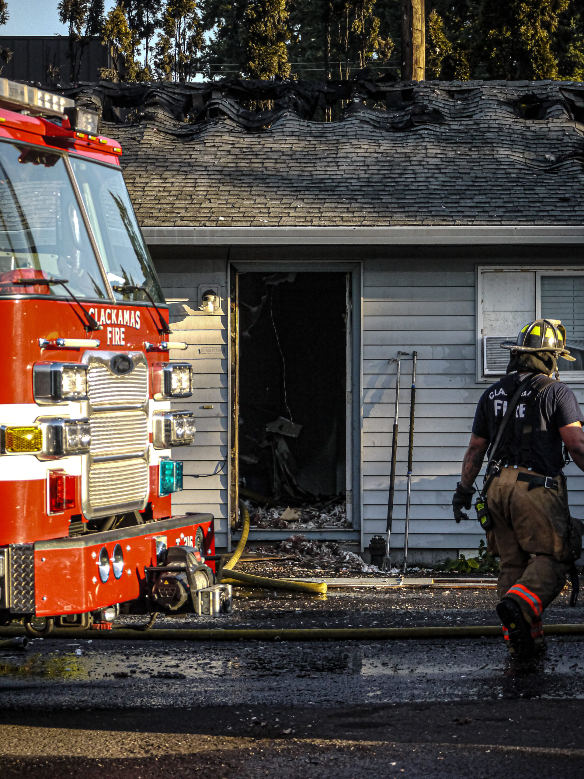 Firefighter walks beside a fire engine and a charred house.