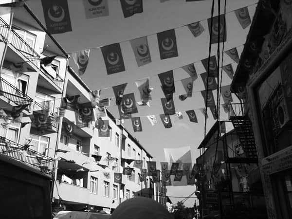 Black-and-white street view with flags strung between apartment buildings and fire escapes.