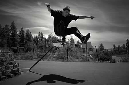A skateboarder performs an airborne trick over pavement in a black-and-white outdoor scene.