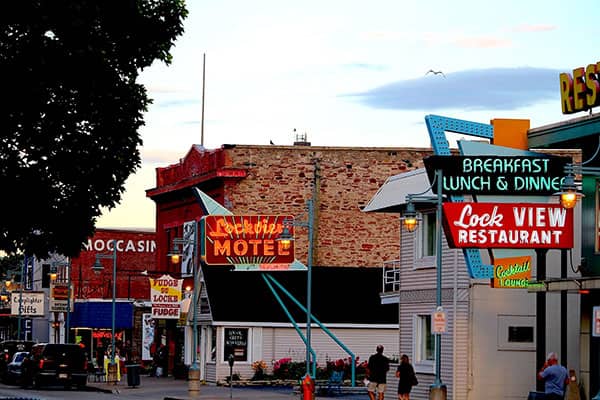 Neon motel and restaurant signs line a small-town street at dusk.