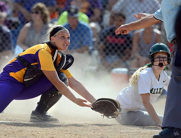 Softball catcher reaches toward a sliding runner as an umpire signals.