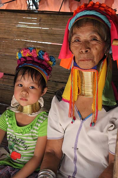 Older woman and young child wear colorful head coverings and brass neck rings.