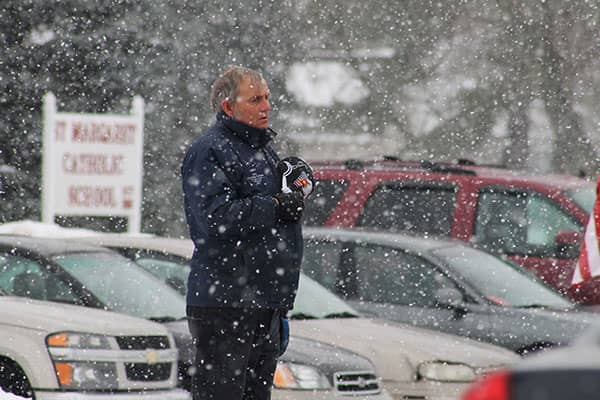 Reporter holds a microphone during heavy snowfall in a parking lot.