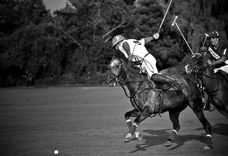 Mounted polo players chase a ball across a field in a black-and-white scene.