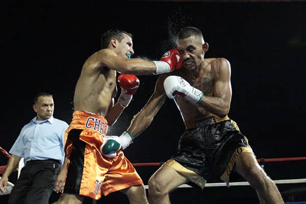 Two boxers exchange punches in a ring while a referee watches.