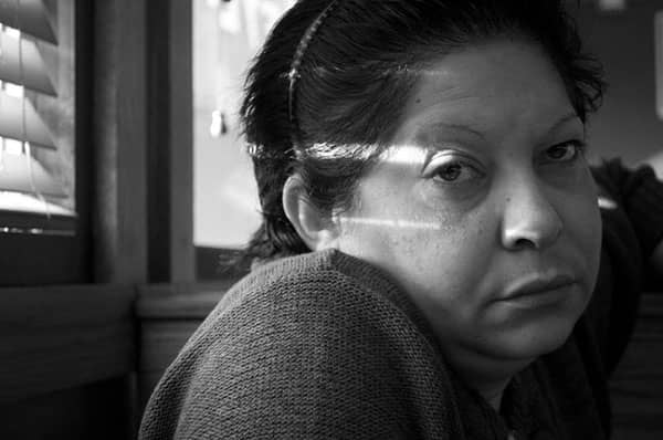 Black-and-white portrait of a woman with window-blind shadows crossing her face.