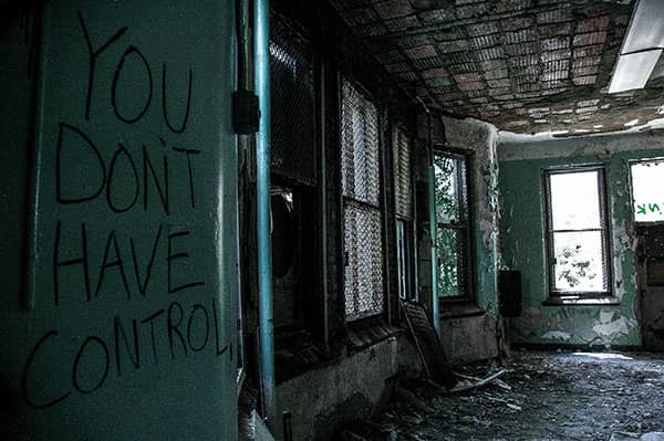 Graffiti reading “YOU DON’T HAVE CONTROL” covers a wall inside a decaying building.