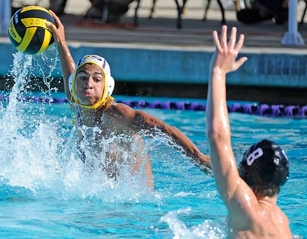 Water polo player raises the ball above splashing water as a defender blocks.