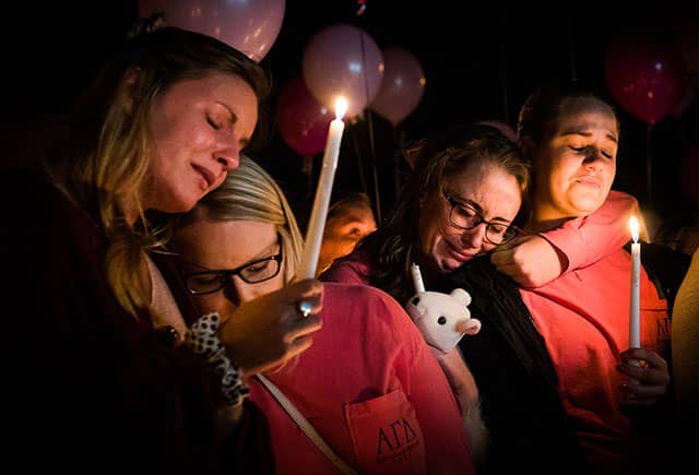 People holding candles embrace during a nighttime vigil illuminated by candlelight.