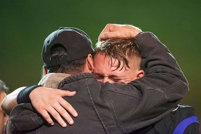 Two men embrace closely on a playing field, one resting a hand overhead.