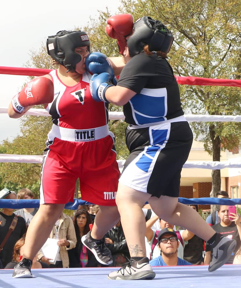Two boxers exchange close-range punches in an outdoor ring surrounded by spectators.