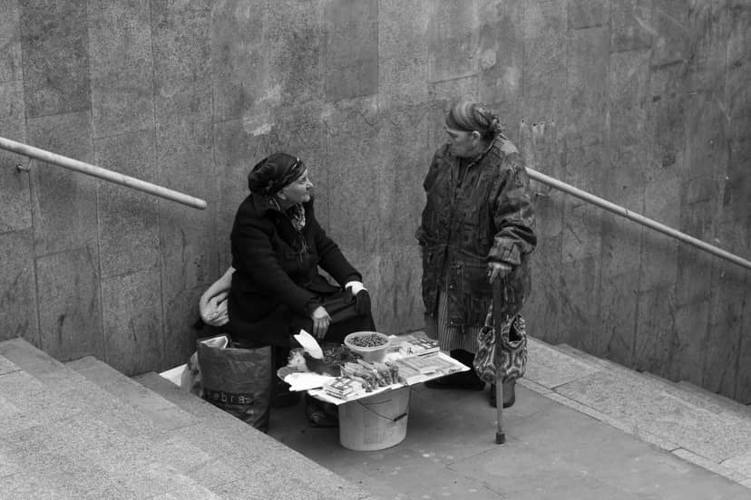 Two women converse beside goods arranged for sale in a concrete stairwell.