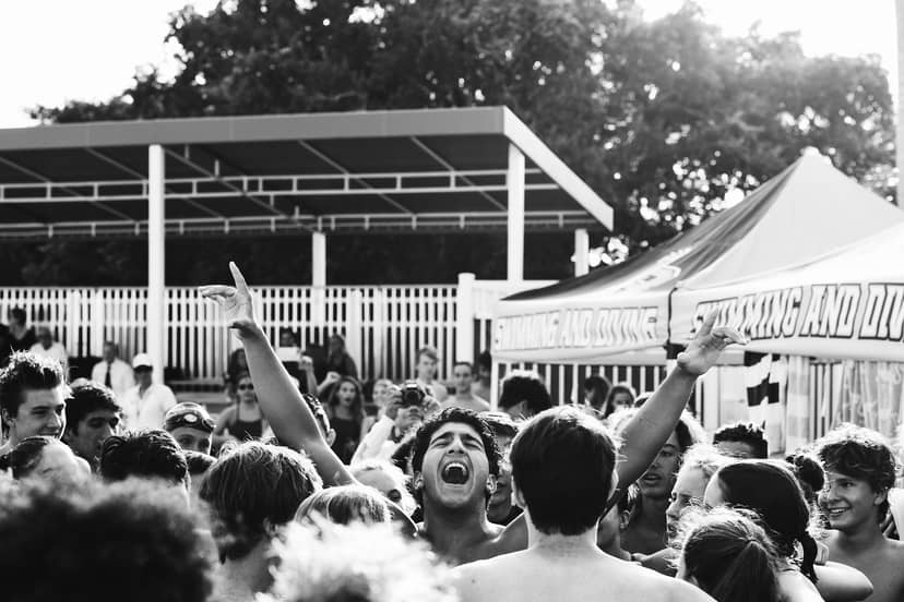 A shirtless person raises both arms while surrounded by a dense outdoor crowd.