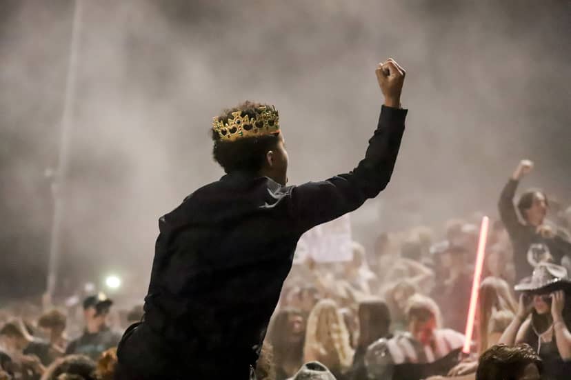 Crowned person raises a fist above a dense nighttime crowd.