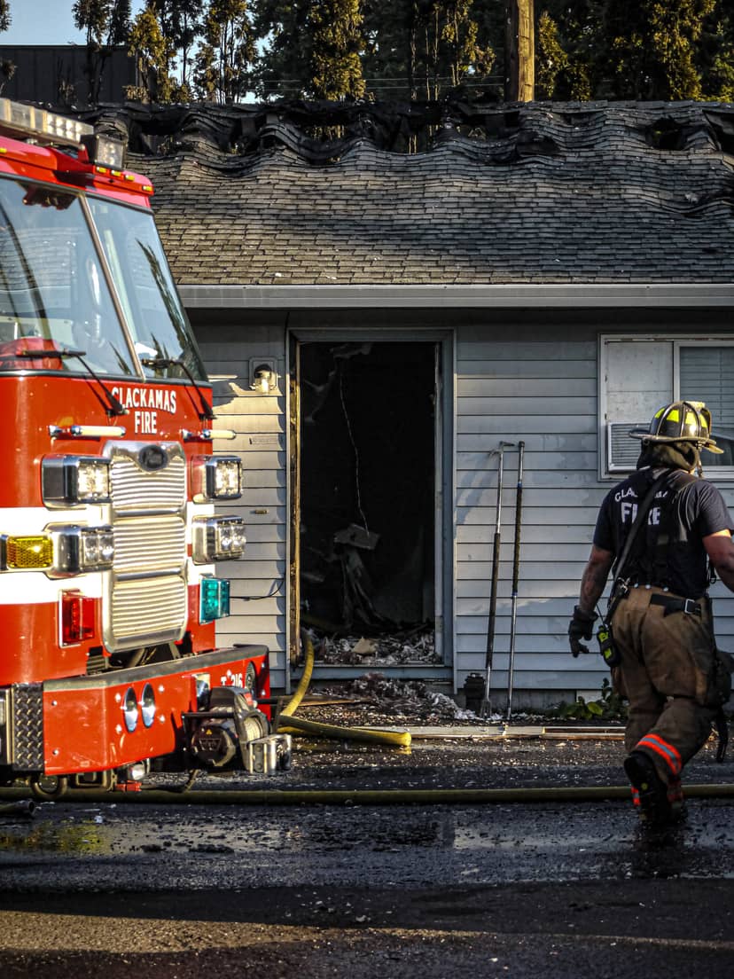 Firefighter walks beside a fire engine and a charred house.