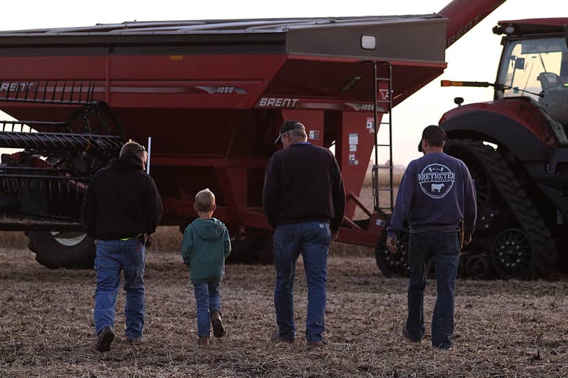Four people, including a child, walk toward red farm machinery.