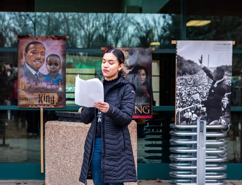 Speaker reads from a page before outdoor Martin Luther King displays.