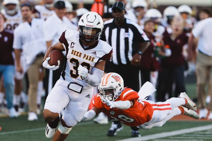 Football ball carrier evades a diving tackler near the sideline.