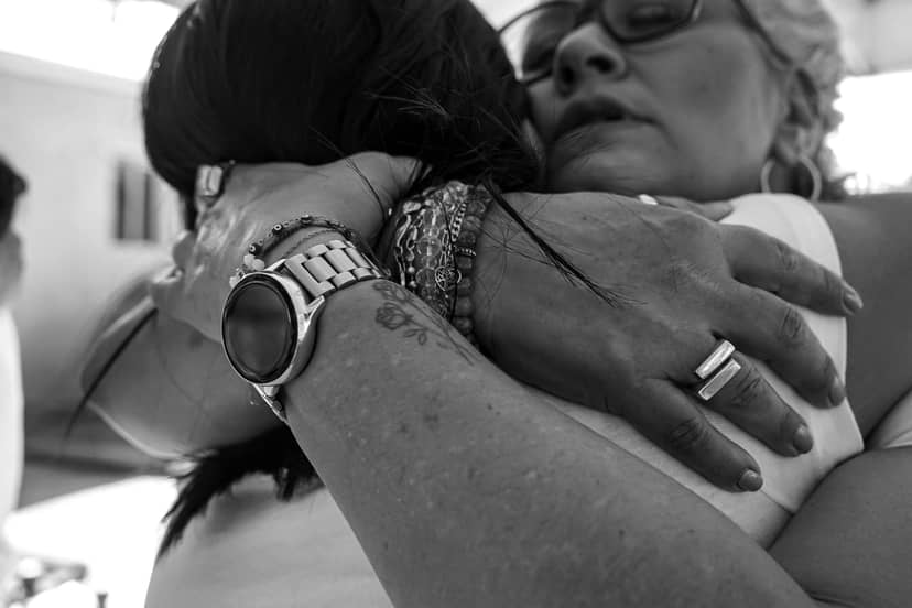 Two people embrace in a black-and-white close-up showing jewelry and a watch.