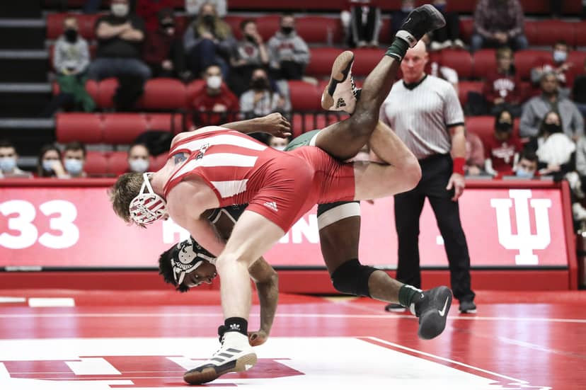 Two wrestlers grapple as one is lifted upside down above the mat.