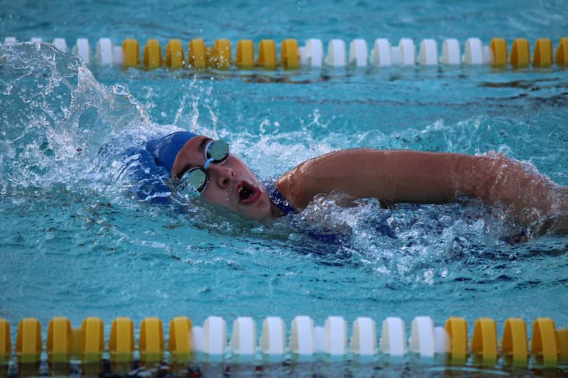 Swimmer in goggles and a blue cap breathes during a freestyle stroke.
