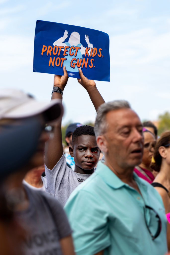 A child holds up a sign that reads "Protect kids not guns"